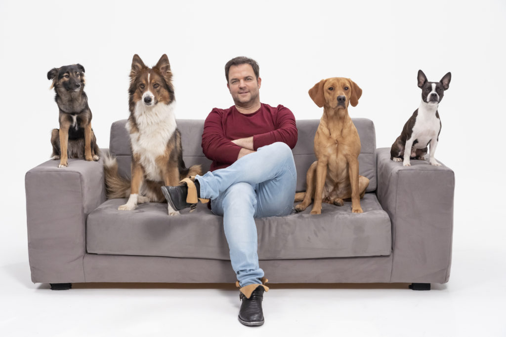 Martin Rütter sitzt von vier Hunden umgeben auf einem Sofa.